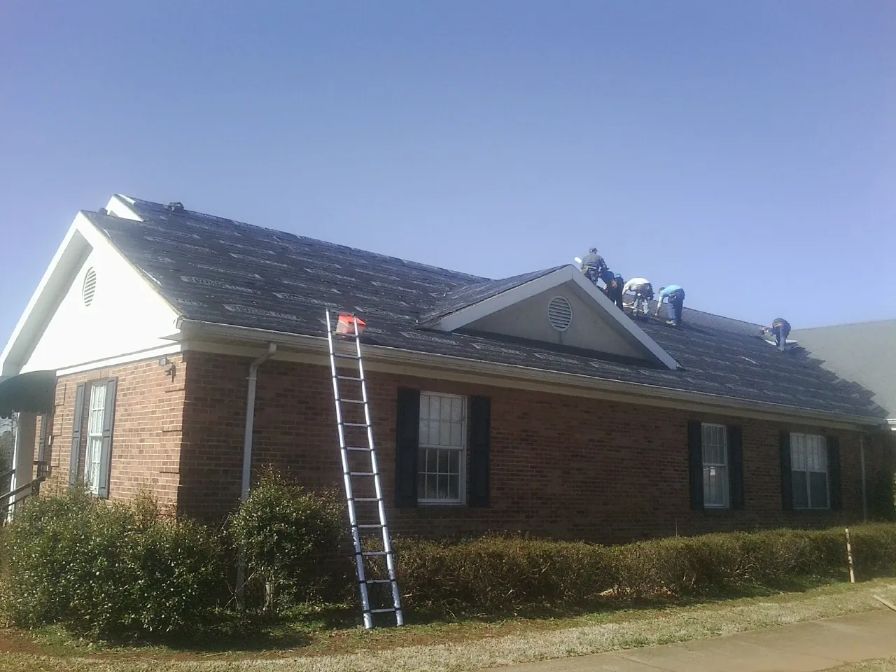 Crew tearing shingles off a brick ranch roof with a ladder set — Metal Roof Repair work by our crew in Boiceville