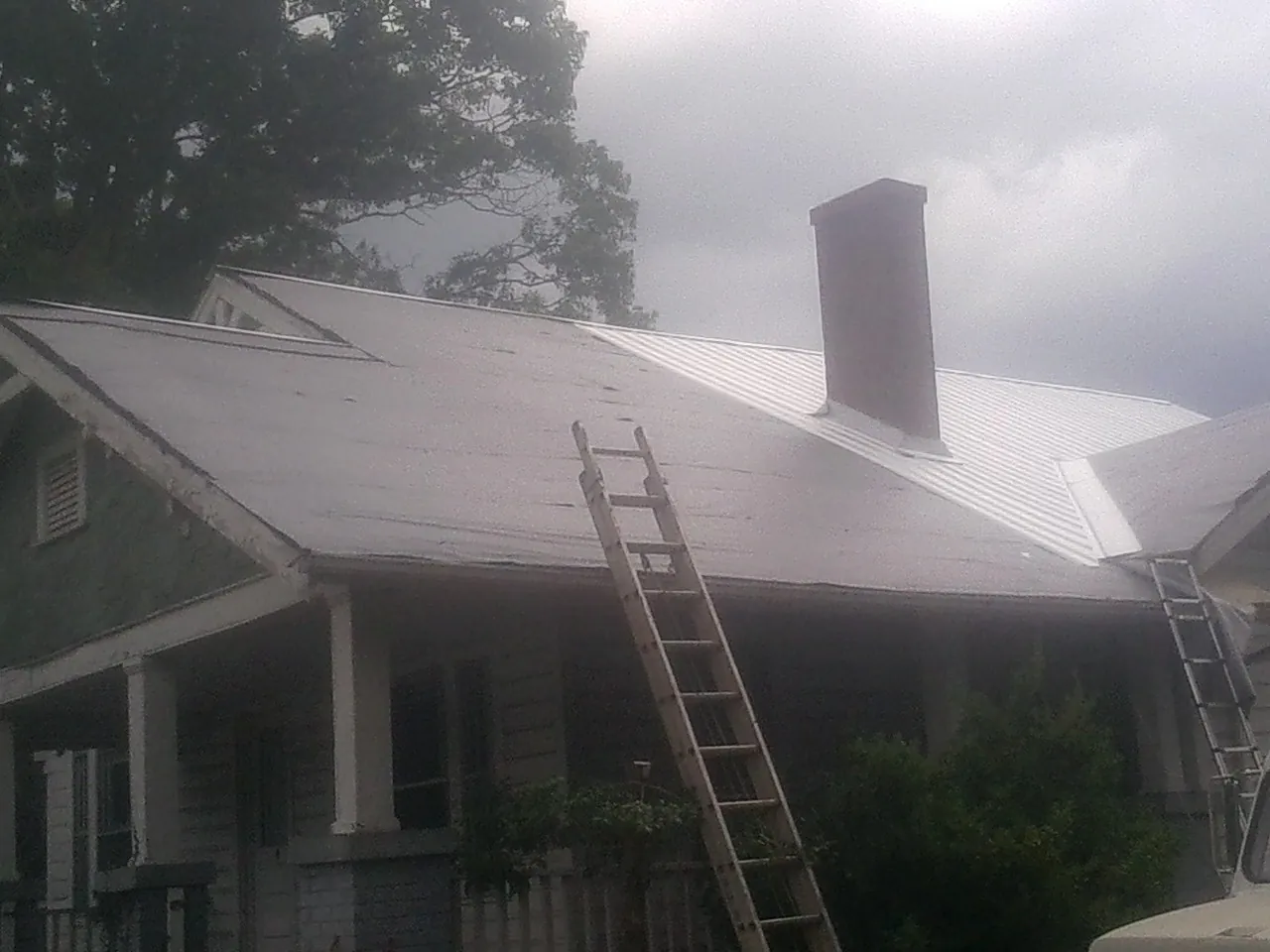 Ladders against a metal roof on an older home with a brick chimney in Boiceville