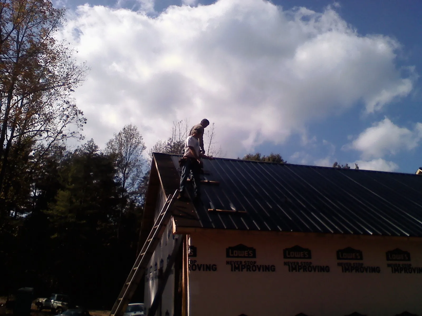 Roofer fastening dark metal panels high against a cloudy sky, from a Roof Inspection job in Boiceville