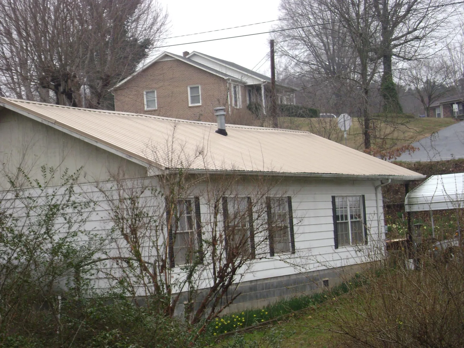 Tan metal roof on a white sided house set into a hillside — Commercial Roofing by Roofing Brothers in Boiceville